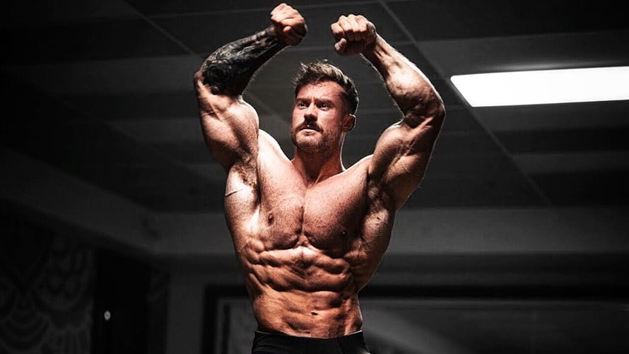 Chris Bumstead Classic Physique Bodybuilding Pose in Dark Gym Setting HD wallpaper