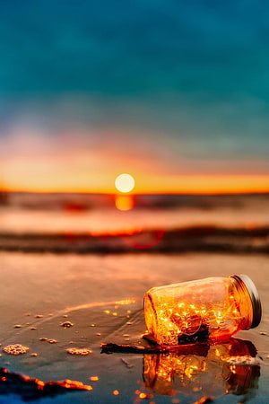 Glowing mason jar with fairy lights on wet sand at sunset HD phone wallpaper