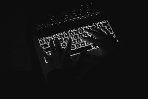 Hands typing on a backlit MacBook Pro keyboard in a dark, moody black and white setting HD wallpaper