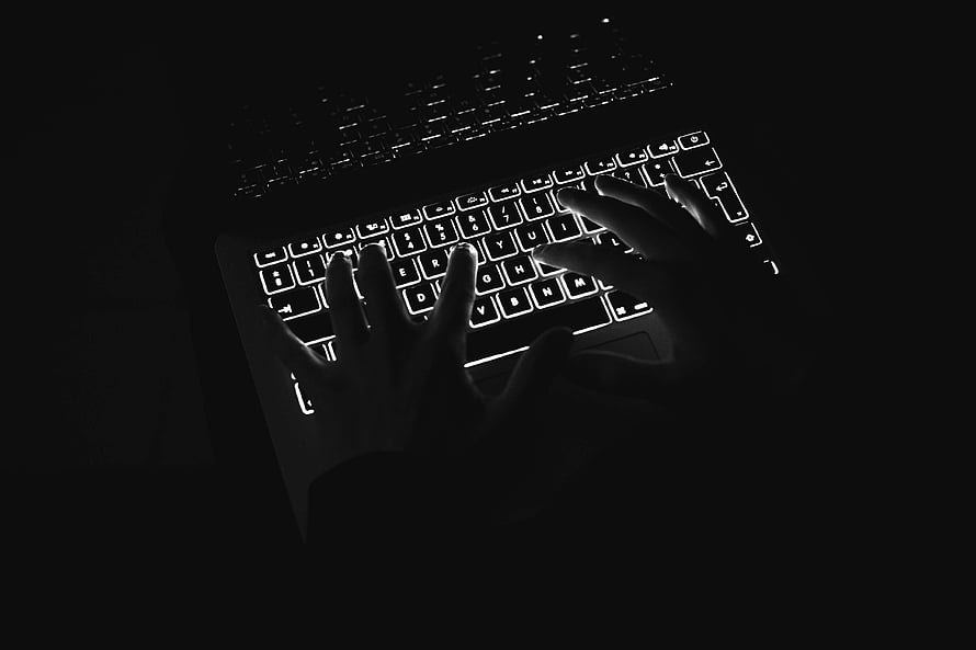 Hands typing on a backlit MacBook Pro keyboard in a dark, moody black and white setting HD wallpaper