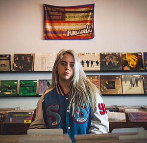 Billie Eilish in a vintage letterman jacket surrounded by vinyl records and a Funkadelic banner HD wallpaper