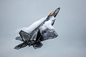 F-22 Raptor Stealth Fighter Jet Banking Through Clouds in Overcast Sky HD wallpaper