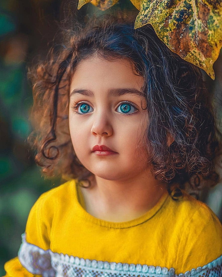 Portrait of a young girl with curly hair and striking blue eyes wearing a yellow top HD phone wallpaper