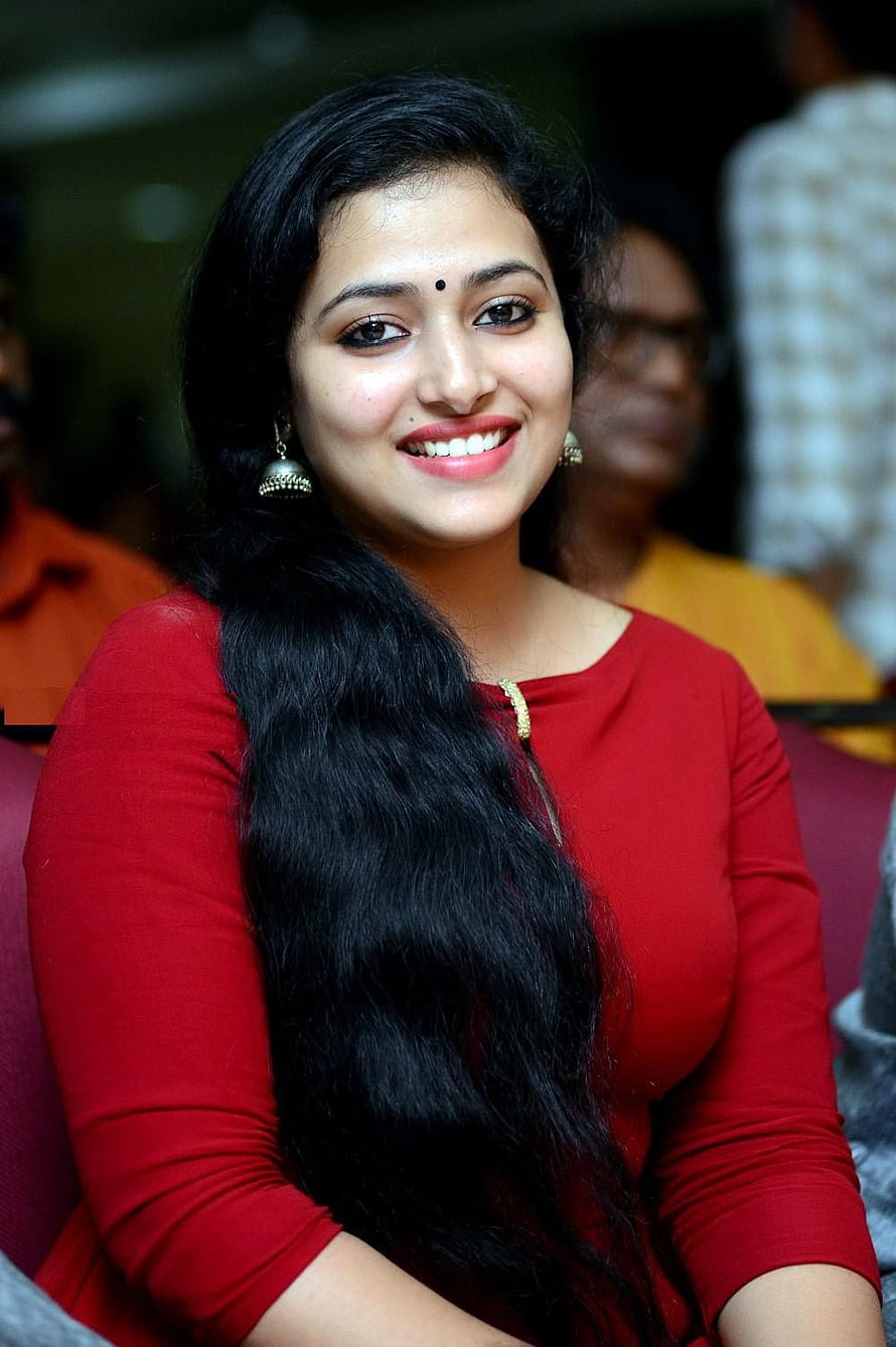 Anu Sithara in a red top with long black hair and traditional gold earrings HD phone wallpaper