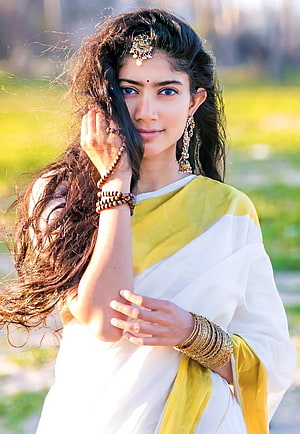 Sai Pallavi in a white and yellow saree with traditional gold jewelry and long flowing hair HD phone wallpaper