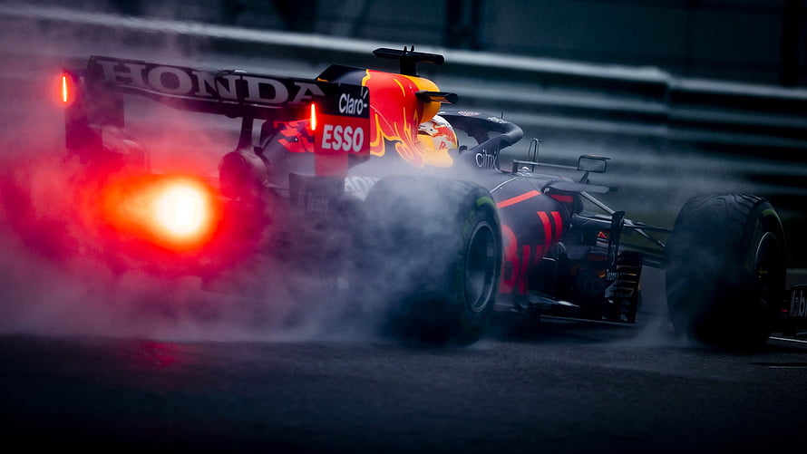 Red Bull Racing Formula 1 car drifting through smoke on a wet track at night HD wallpaper