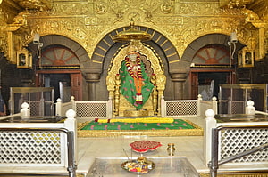 Sai Baba shrine with golden canopy, green dhoti, and marigold garlands in ornate temple sanctum HD wallpaper