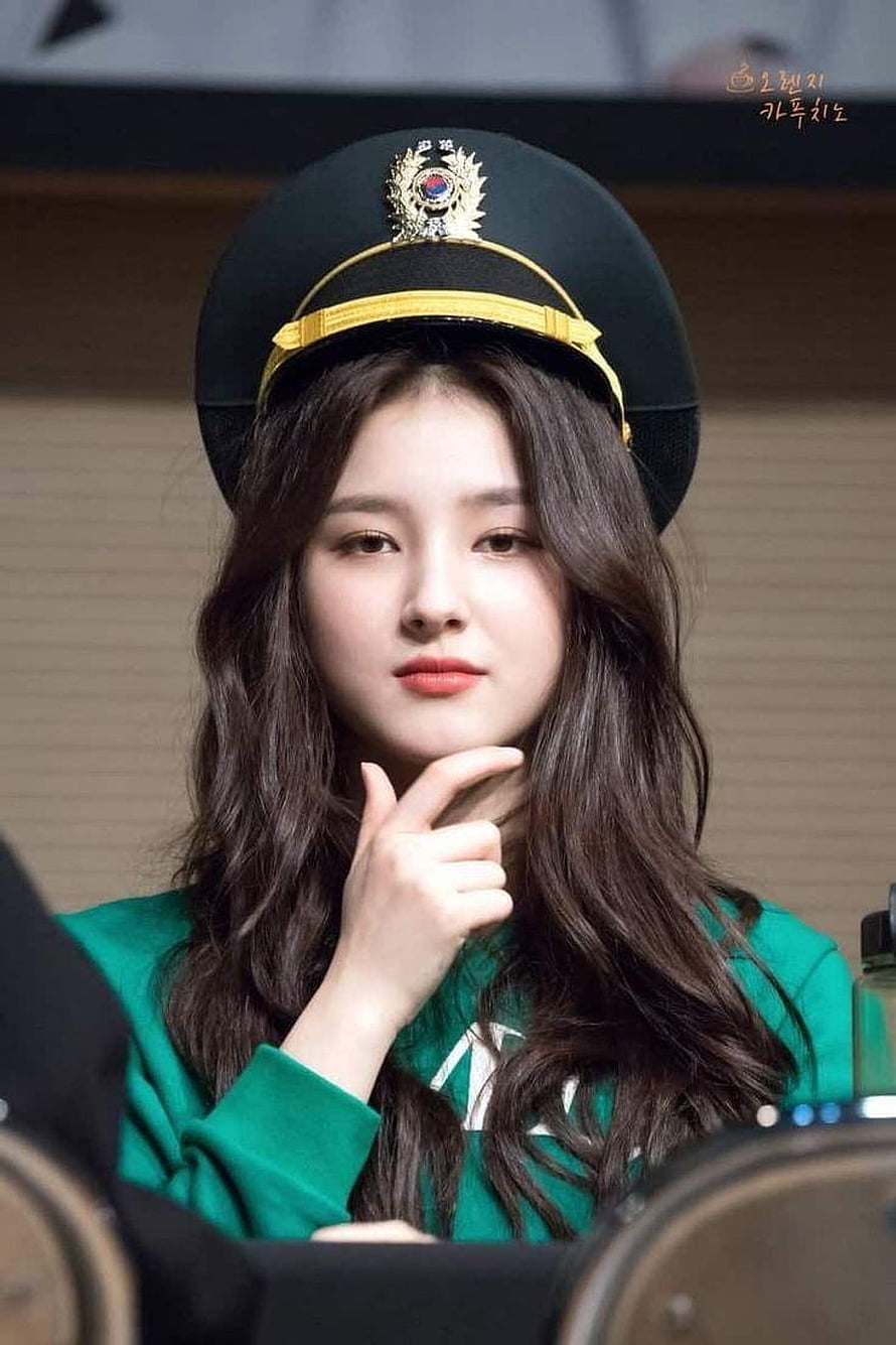 Nancy wearing a black military-style cap with gold trim and a green top, hand resting on chin HD phone wallpaper