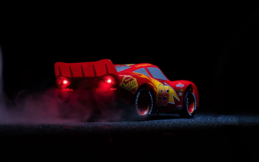 Lightning McQueen from Cars 3 drifting with smoke and glowing red taillights on a dark track HD wallpaper