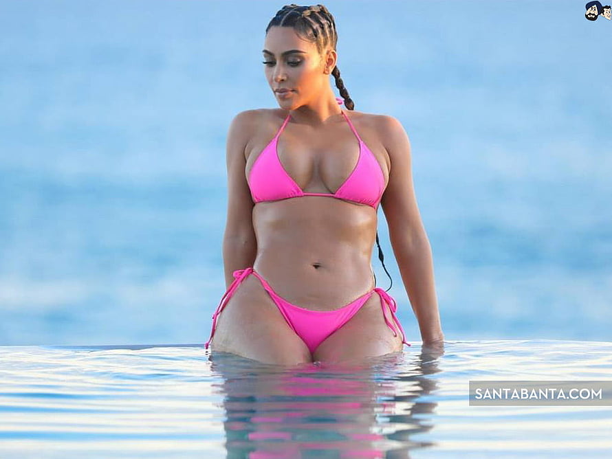 Kim Kardashian in a bright pink bikini standing in a calm infinity pool with a soft blue sky background HD wallpaper