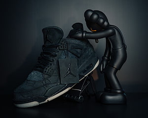 KAWS Companion Figure Leaning on Black Jordan 4 Sneaker HD wallpaper