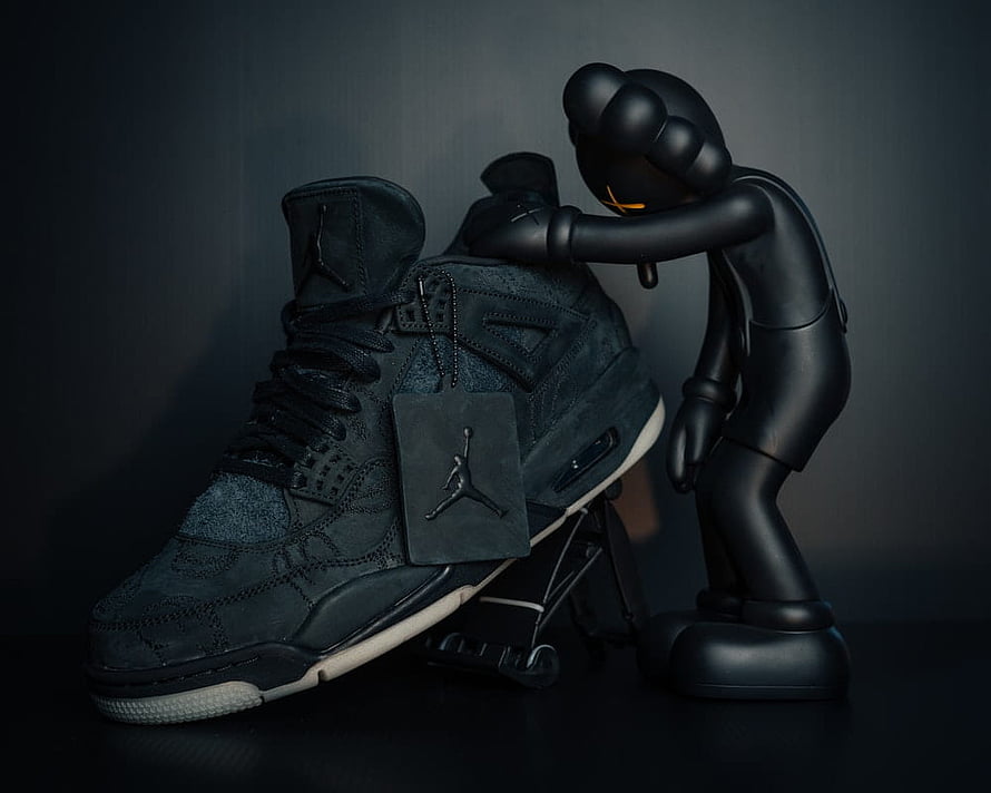 KAWS Companion Figure Leaning on Black Jordan 4 Sneaker HD wallpaper