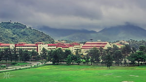 IIT Guwahati campus buildings with red roofs set against misty green hills under a cloudy sky HD wallpaper