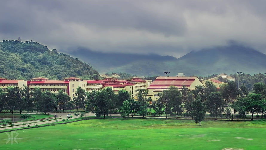 IIT Guwahati campus buildings with red roofs set against misty green hills under a cloudy sky HD wallpaper