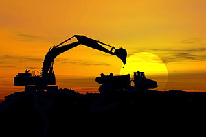 Excavator and Dump Truck Silhouetted Against a Golden Sunset at a Construction Site HD wallpaper