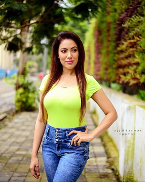 Munmun Dutta in a lime green top and blue jeans on a lush garden pathway HD phone wallpaper