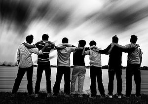 Seven friends standing arm in arm by a lake under a dramatic cloudy sky in black and white HD wallpaper