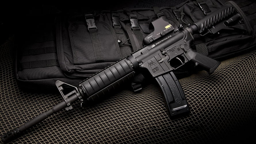 Black Tactical Rifle with Red Dot Sight Resting on Military Gear and Mesh Surface HD wallpaper