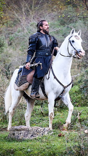 Ertugrul Gazi in Dark Armor Riding a White Horse Through a Forest HD phone wallpaper