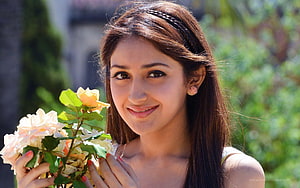 Young woman with long brown hair holding a bouquet of pale roses in a sunlit garden HD wallpaper