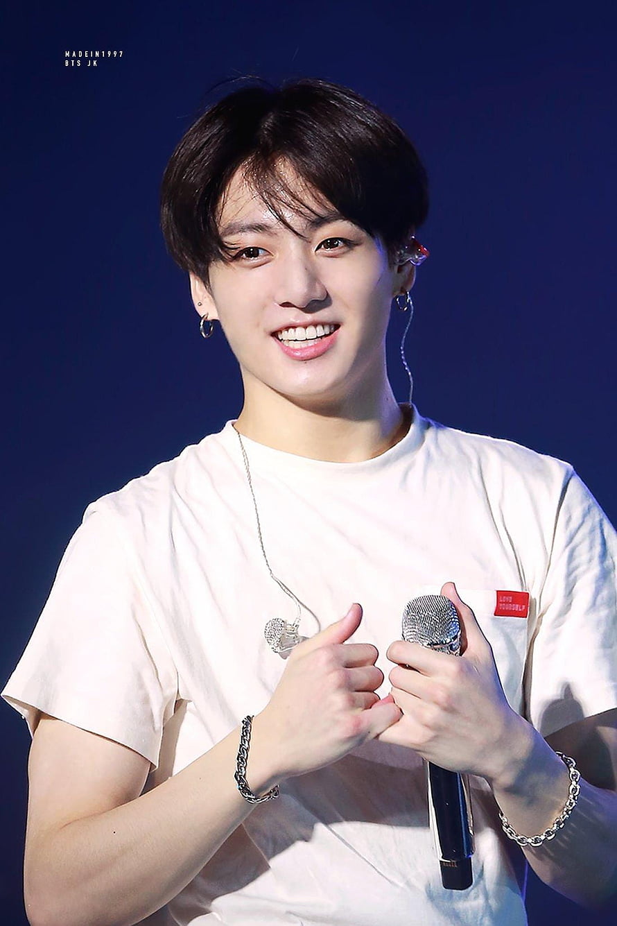 Jungkook from BTS smiling on stage in a white t-shirt holding a microphone HD phone wallpaper