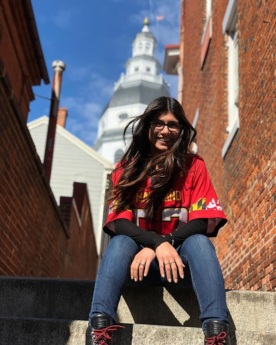 Young woman in red Maryland jersey sitting on stone steps with historic white steeple in background HD phone wallpaper