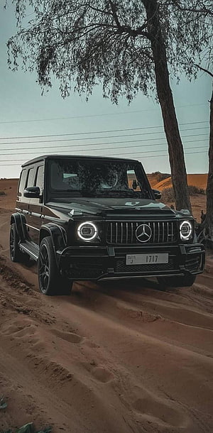 Black Mercedes-Benz G-Class SUV parked on a sandy desert trail under a tree HD phone wallpaper