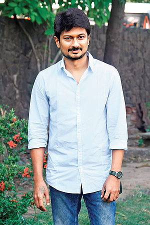 Udhayanidhi Stalin in a light blue shirt and jeans standing outdoors with greenery HD phone wallpaper