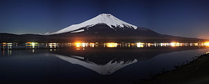 Snow-Capped Volcano Reflected in a Calm Lake at Night with Distant City Lights HD wallpaper