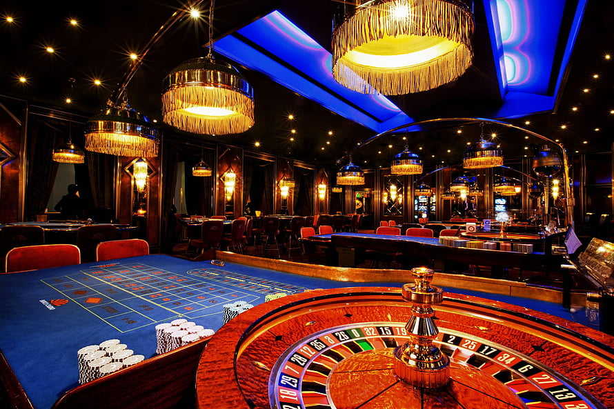 Luxury Casino Gaming Floor With Roulette Wheel And Blue Card Table Under Golden Chandeliers HD wallpaper