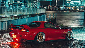 Red Mazda RX-7 JDM Coupe Parked on Wet Cobblestones at Night with City Skyline HD wallpaper