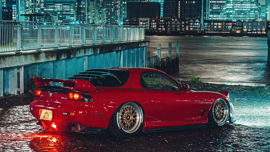 Red Mazda RX-7 JDM Coupe Parked on Wet Cobblestones at Night with City Skyline HD wallpaper