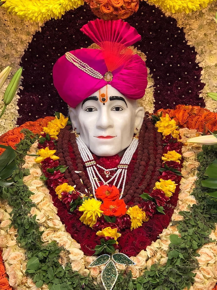 Shri Gajanan Maharaj adorned in vibrant floral garlands and a traditional pink turban HD phone wallpaper