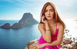 Jia Lissa in a vibrant pink dress posing on a rocky coastal cliff overlooking the sea HD wallpaper