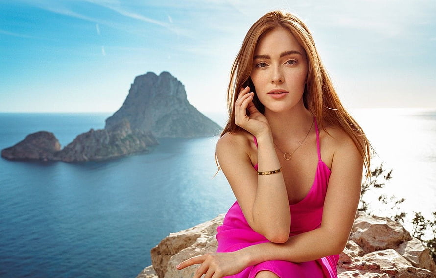Jia Lissa in a vibrant pink dress posing on a rocky coastal cliff overlooking the sea HD wallpaper