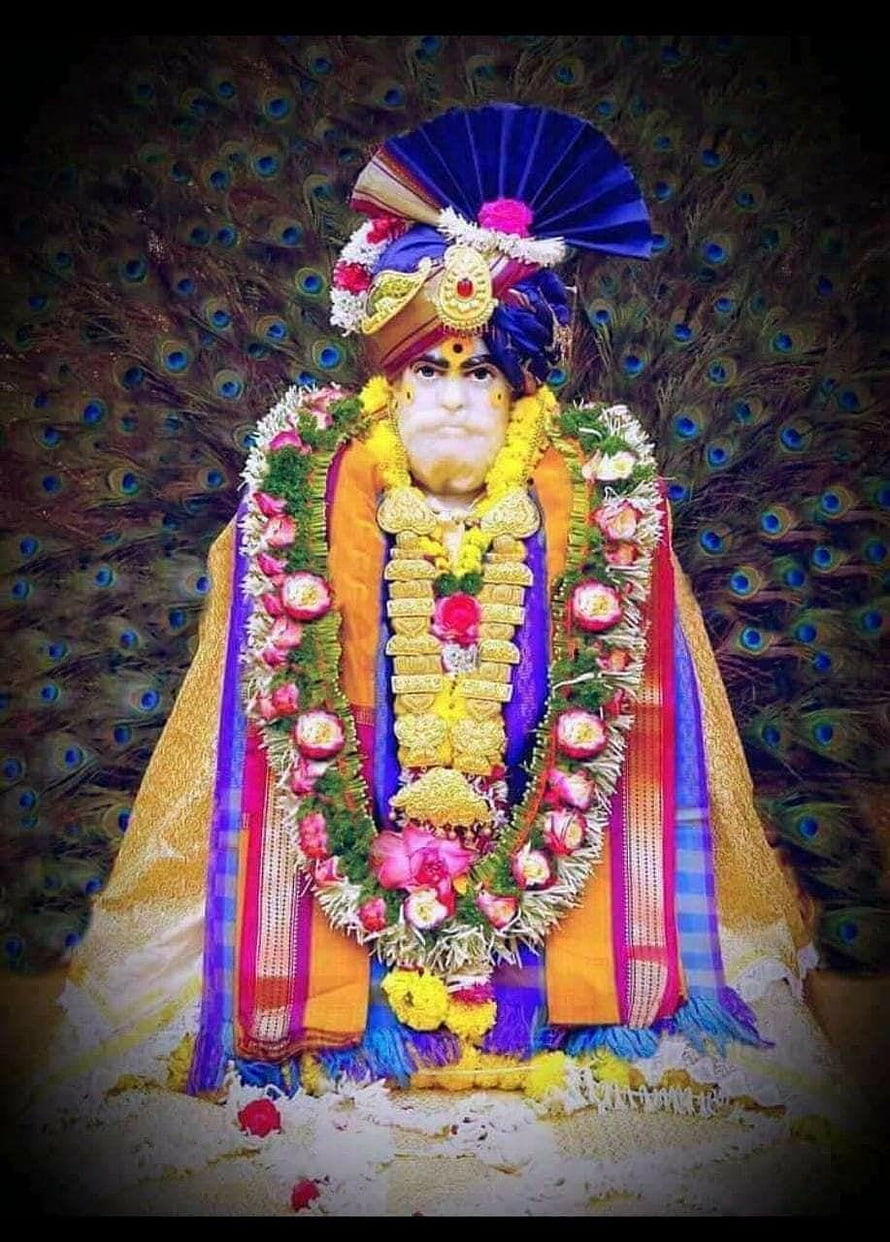 Shankar Maharaj adorned in vibrant silk garments and floral garlands against a peacock feather backdrop HD phone wallpaper