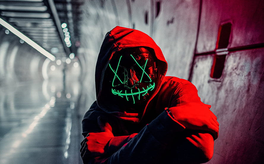 Figure in red hoodie wearing a glowing green neon mask in a dim tunnel HD wallpaper