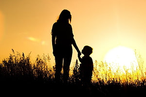 Silhouette of a mother and child holding hands in a field at golden hour sunset HD wallpaper