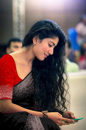 Sai Pallavi in a red and black saree looking at a smartphone HD phone wallpaper