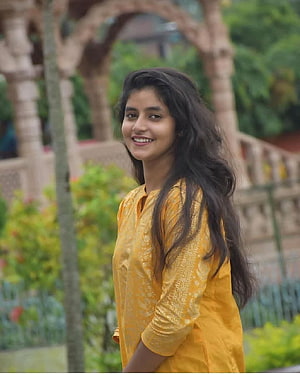 Sanchita Basu in a yellow kurta standing in a garden with stone arches HD phone wallpaper