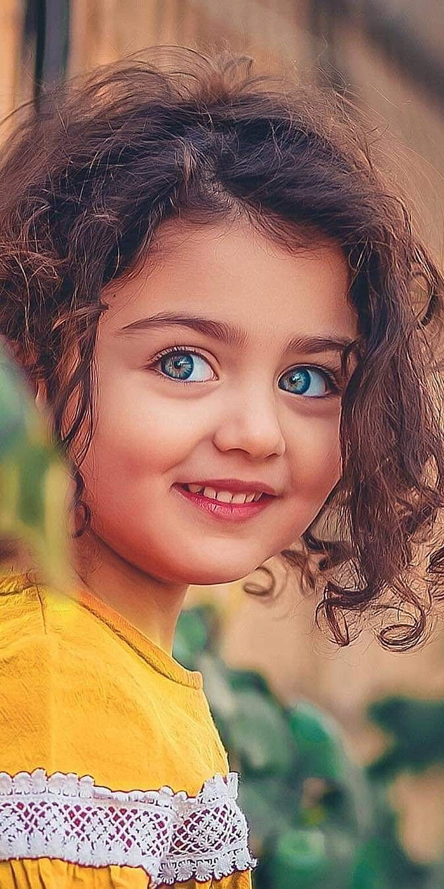 Smiling young girl with curly brown hair and bright blue eyes wearing a yellow top HD phone wallpaper