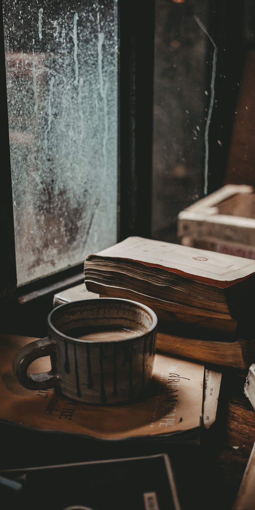 Cozy coffee mug and vintage books on a windowsill with a rainy winter view HD phone wallpaper