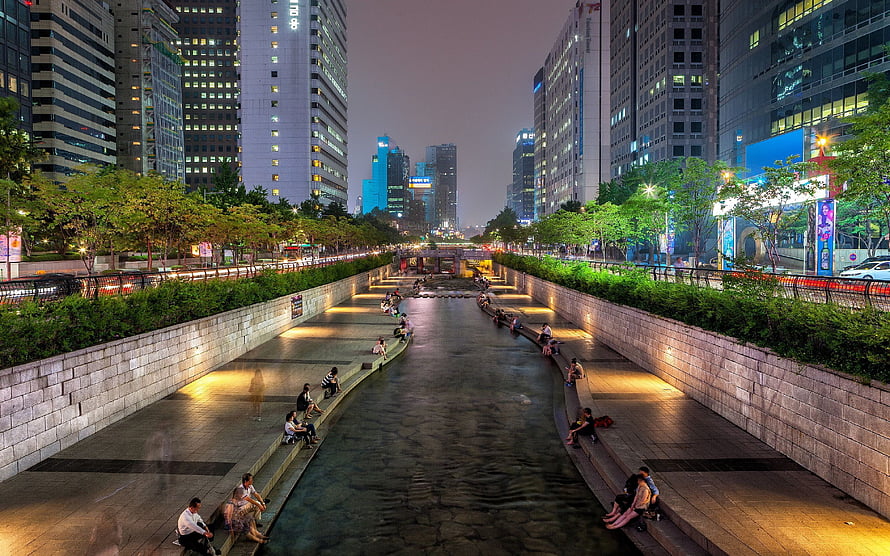 Cheonggyecheon Stream at Dusk in Seoul with City Skyline and Pedestrians HD wallpaper