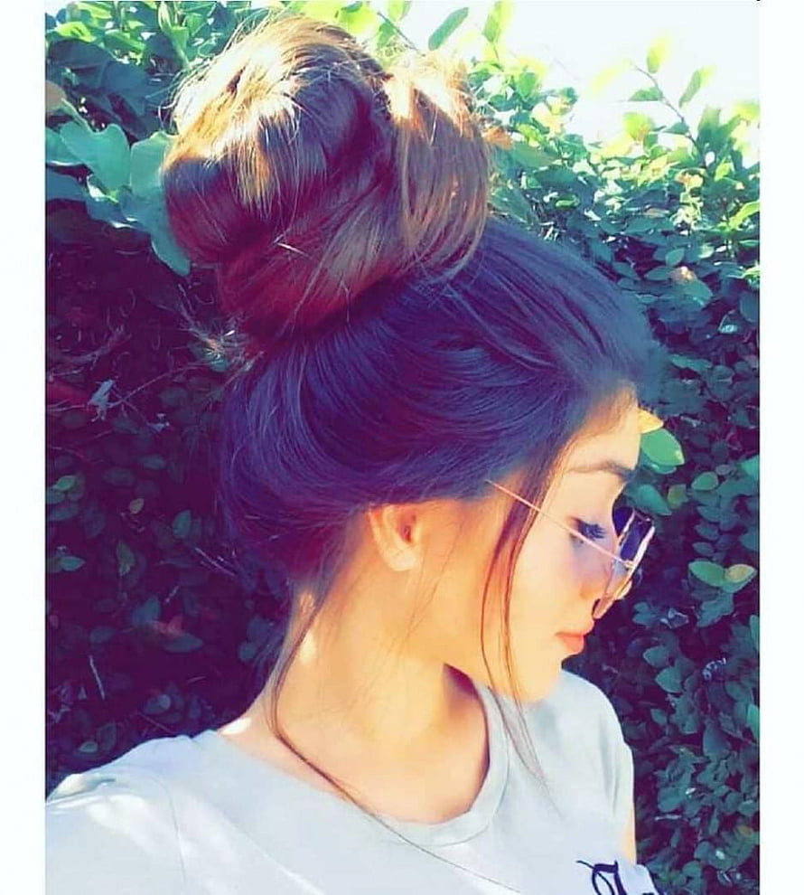Young woman with a high messy bun hairstyle and sunglasses in profile against a leafy green hedge HD phone wallpaper
