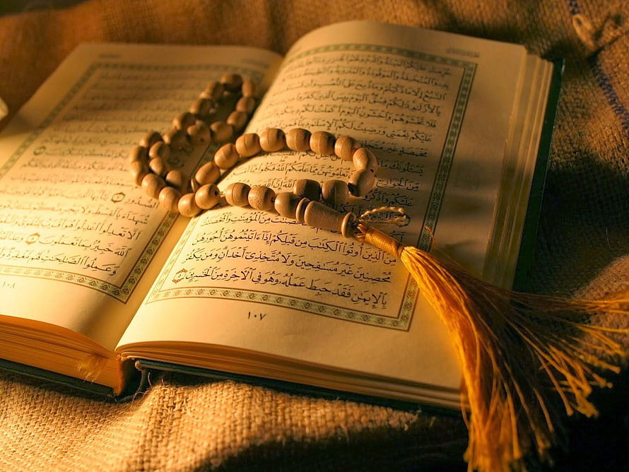 Open Quran with wooden prayer beads and golden tassel on textured fabric HD wallpaper