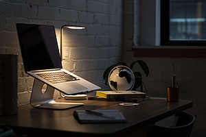 Cozy Home Office Setup With MacBook On Stand, Desk Lamp, And Books Against White Brick Wall HD wallpaper