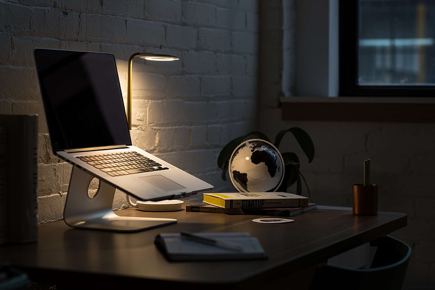 Cozy Home Office Setup With MacBook On Stand, Desk Lamp, And Books Against White Brick Wall HD wallpaper