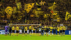 Borussia Dortmund players line up on the pitch with fans waving yellow and black flags in the stands HD wallpaper