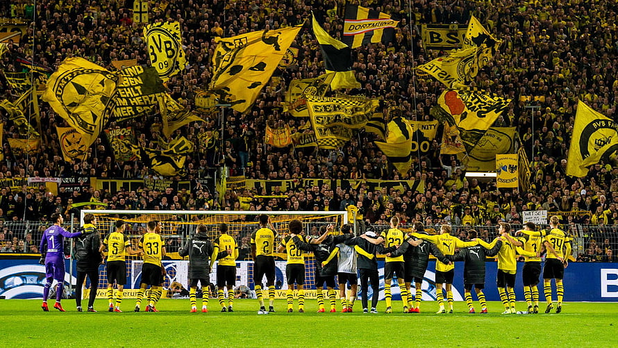 Borussia Dortmund players line up on the pitch with fans waving yellow and black flags in the stands HD wallpaper
