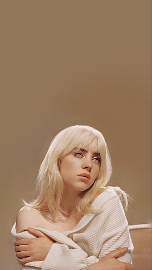 Billie Eilish in a white off-shoulder sweater with a contemplative expression against a warm beige background HD phone wallpaper